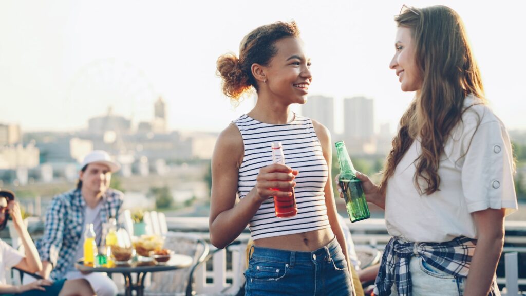 Two women talking and drinking on a rooftop.