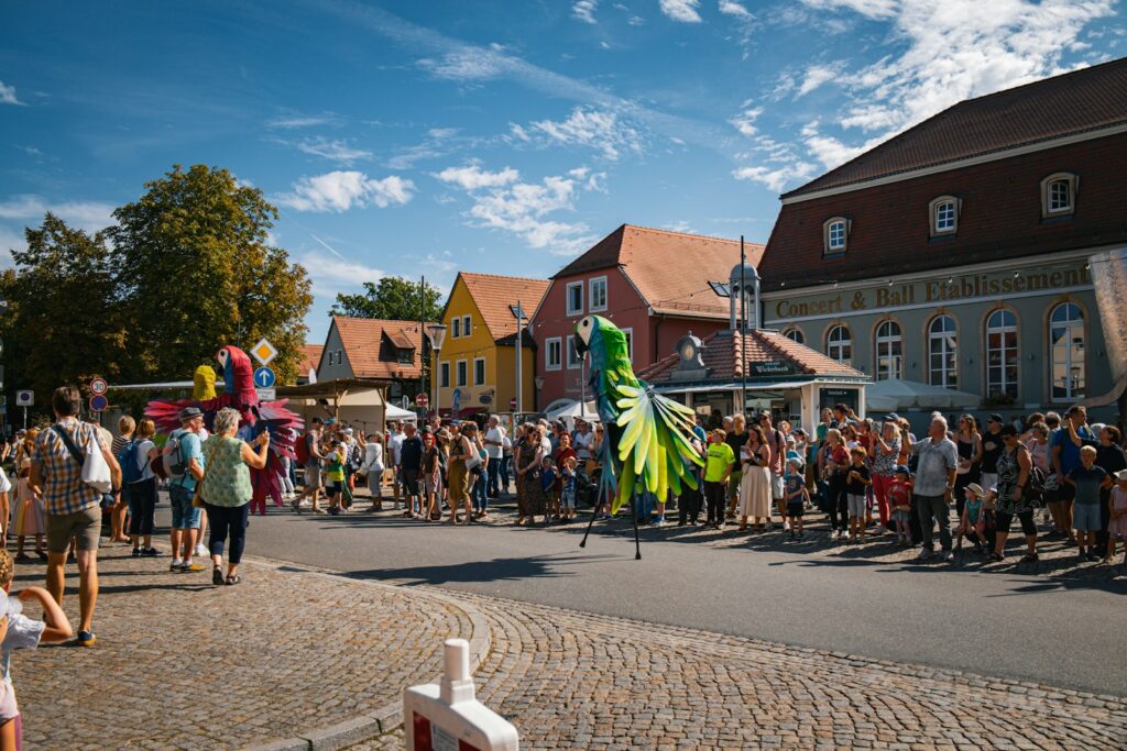 People watch a parade with a large green bird costume.